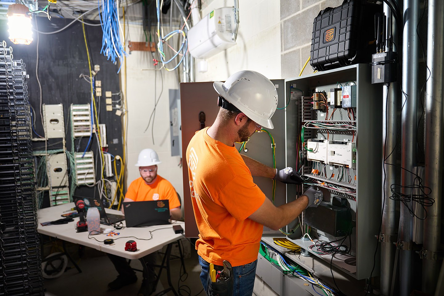 TC Controls technicians wiring a building automation control panel in a mechanical room